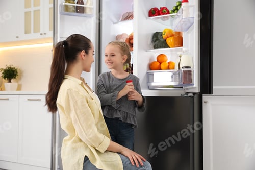 Preview: Young mother with daughter near open refrigerator in kitchen