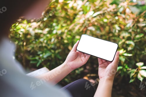 Preview: Mockup image of a woman holding mobile phone with blank white desktop screen in the outdoors