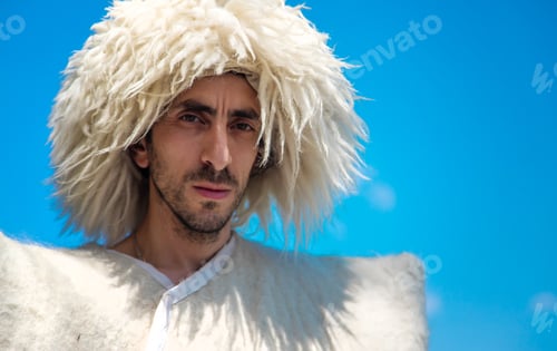 Preview: A Georgian man in a hat against the background of mountains and the sky. Selective focus.