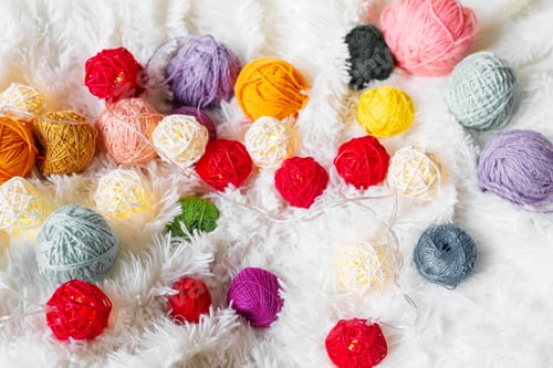 Preview: Bright multicolored knitting yarn and a luminous garland in the form of balls lie on fluffy blanket.