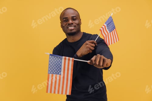 Preview: Young Man Holding Two United States Flags on Yellow Background