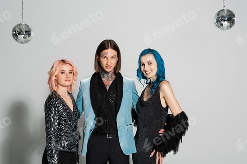 Preview: tattooed queer person looking at camera near elegant nonbinary friends smiling at camera on grey