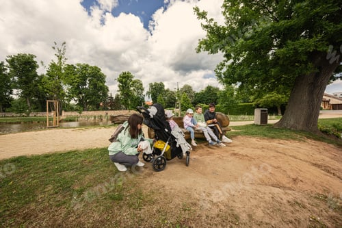 Preview: Mother with kids sitting and having rest in wooden bench outdoor in park.