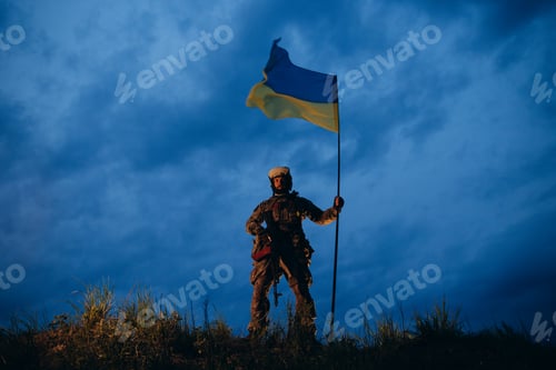 Preview: Armed Ukrainian soldier holding a national flag in the evening