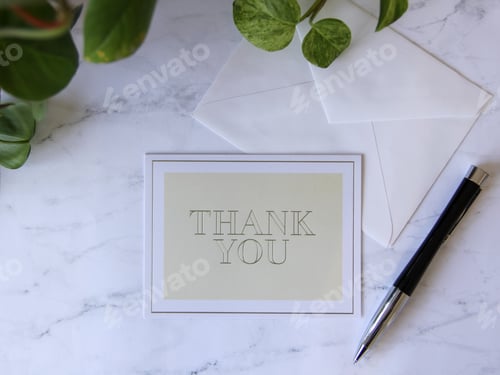 Preview: Flat lay of Thank you card on counter with green plant pen & envelope while writing thank you notes