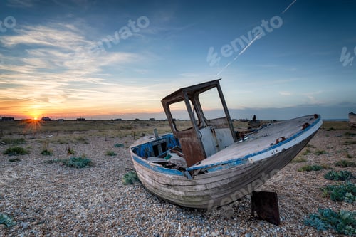 Preview: An old abandoned wooden fishing boat with nets washed up on a shingle beach