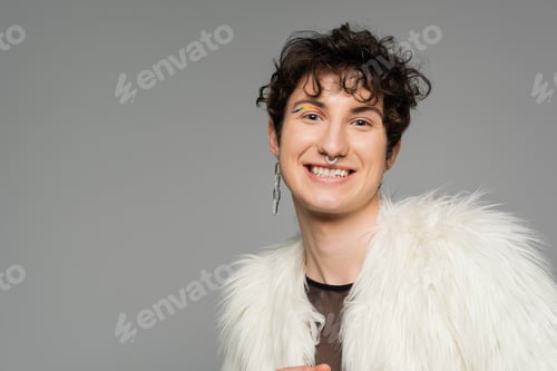Preview: overjoyed pansexual model in silver accessories and white faux fur jacket smiling at camera isolated