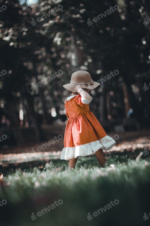 Preview: A little girl wearing a red dress and a hat walking in a park