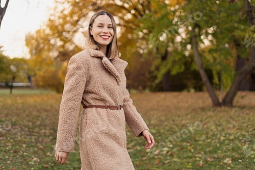 Preview: Smiling woman walking in the autumn park wearing a long coat