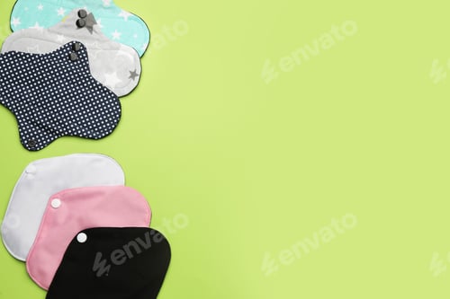Preview: Many reusable cloth menstrual pads on green background, flat lay. Space for text