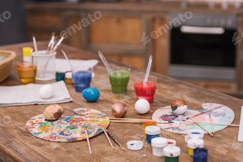 Preview: painted chicken eggs with paints and brushes on wooden table, easter concept