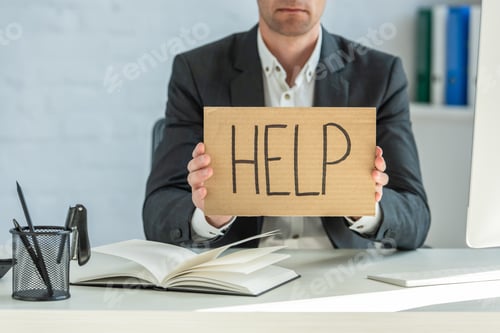 Preview: Cropped view of businessman holding cardboard with help lettering, while sitting at table on blurred