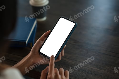 Preview: Close up woman hand holding a smartphone blank white screen at office wooden table.