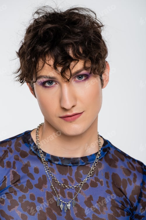 Preview: portrait of brunette queer person with makeup looking at camera isolated on grey