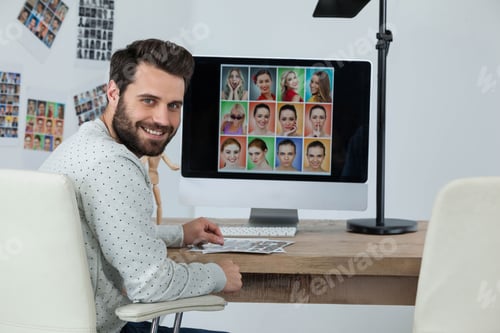 Preview: Man reviewing printed contact sheets at wooden desk in creative studio, with grid of portraits