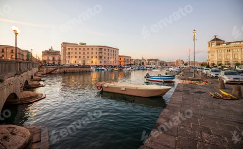 Preview: Fishing boats on the water in Ortigia island with the cityscape of Syracuse in the evening