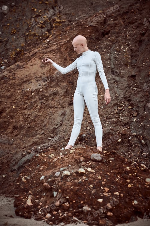 Preview: Full length portrait of young hairless girl with alopecia in white suit holding handful of earth