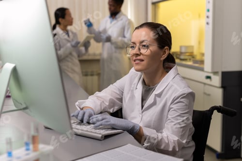 Preview: Smiling woman in workwear looking at computer screen while working in lab
