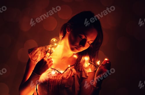 Preview: Woman holding Christmas lights in her hands and dreaming. Reverie