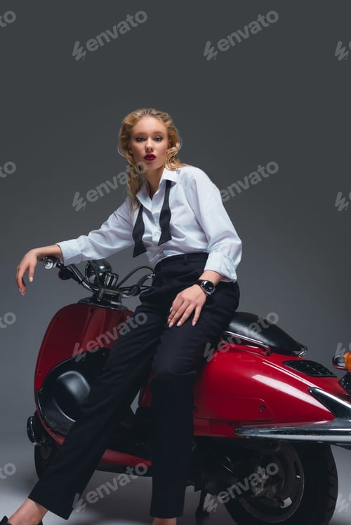 Preview: beautiful fashionable model posing on red retro scooter on grey