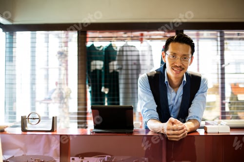 Preview: Japanese salesman standing at counter in clothing store, smiling at camera.