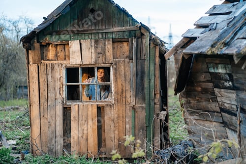 Preview: girl looks out the window from an old wooden house