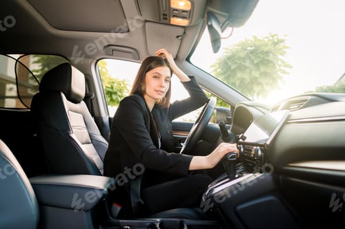 Preview: Side view of young beautiful business woman sitting in her car on driver seat and looking at camera
