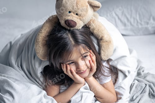 Preview: Little cute girl in bed with a teddy bear early in the morning.