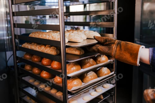 Preview: close up view of woman holding holding rack of rolls in a bakery.