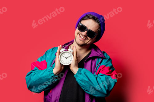 Preview: Funny guy in 80s style jacket and sunglasses holds alarm clock on red backgorund
