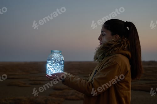 Preview: Girl is holding fairy lights in a jar on winter dry landscape
