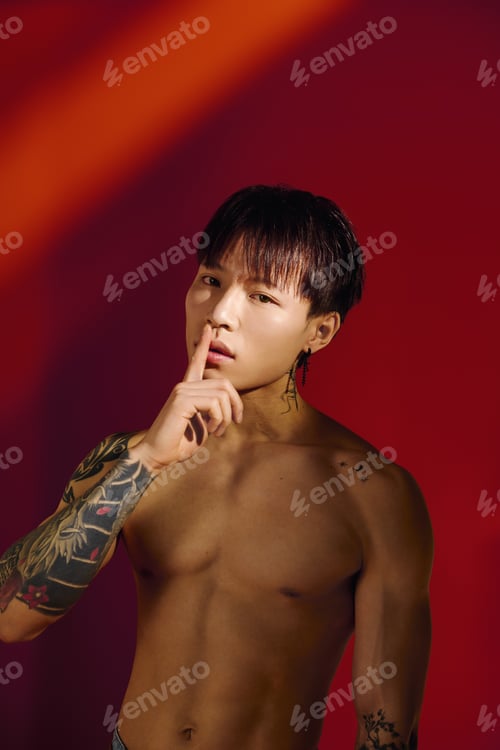 Preview: Tattooed young man poses confidently against a vibrant red background in an artistic shot