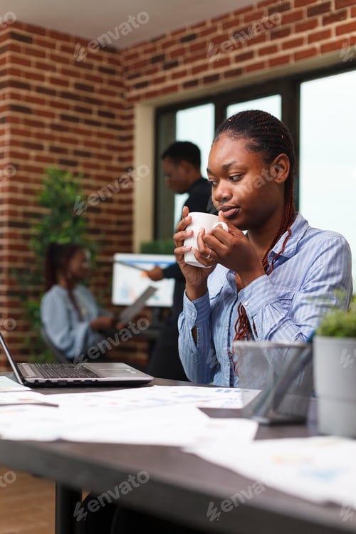 Preview: Marketing agency office worker having a cup of coffee while looking at work laptop.