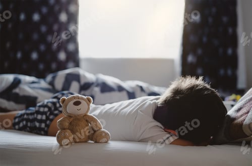 Preview: Cute Teddy bear sitting on bed next to child boy with morning light.