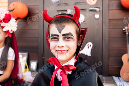 Preview: Cheerful boy with painted face in costume of devil sitting in front of camera