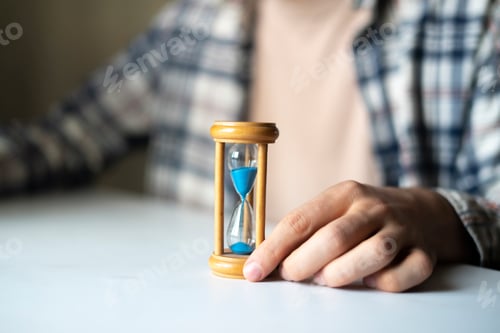 Preview: a businessman sitting on the workplace, hand holding hourglass as the time is money concept