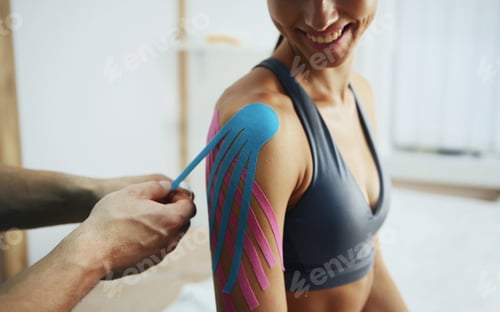 Preview: Doctor helps woman by shoulder treatment with kinesio tape