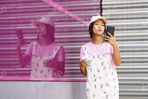 Preview: Young Asian woman with smartphone and coffee near pink wall