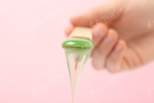 Preview: Woman holding spatula with hot depilatory wax on light background, closeup