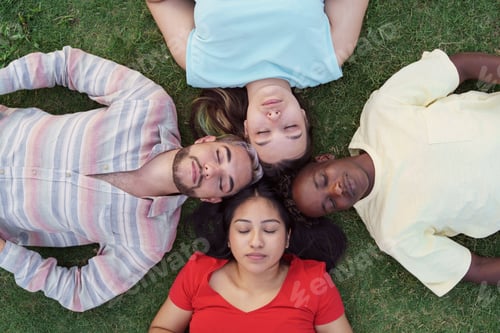 Preview: Relaxed young friends lying together on green grass with eyes closed, dreaming together