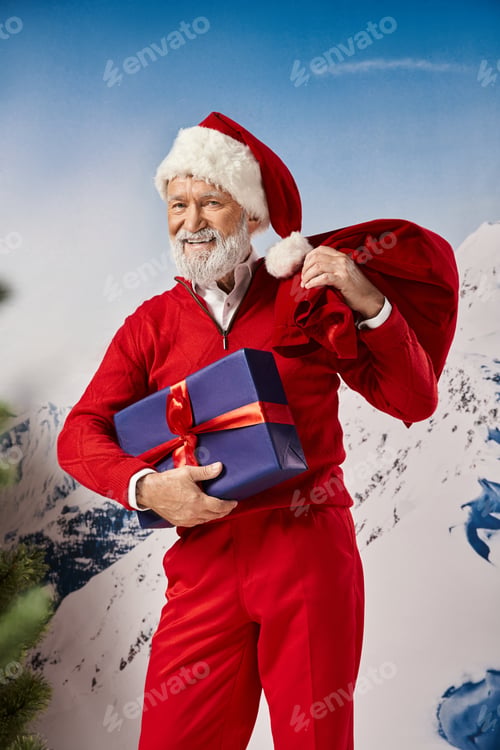 Preview: cheerful man in Santa costume smiling sincerely and holding present and gift bag, winter concept