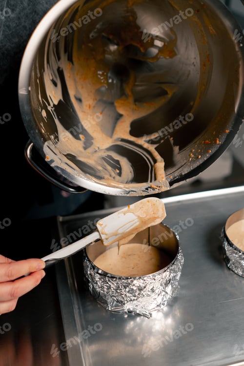 Preview: close up hands female baker in a professional kitchen pours dough into layers of cake molds