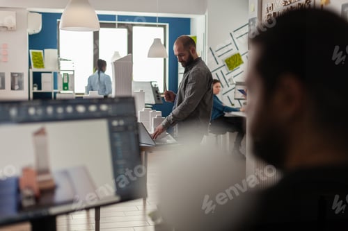 Visualização: Engenheiro olhando plantas no laptop na mesa com modelo arquitetônico
