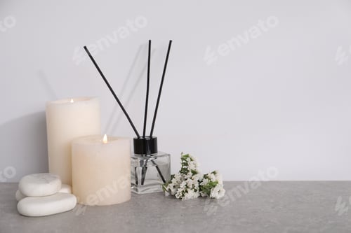 Vista previa: Composición de spa con velas encendidas y difusor de láminas sobre mesa gris claro, espacio para texto