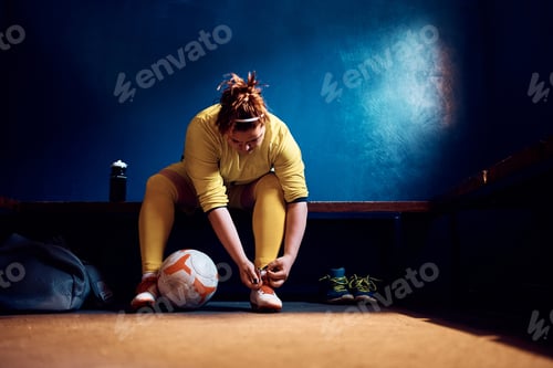 Preview: Female goalie getting reading for match and tying shoelaces in locker room.