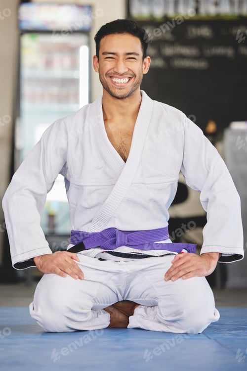 Preview: Full length portrait of a handsome young man kneeling in full jiu jitsu gi in the gym