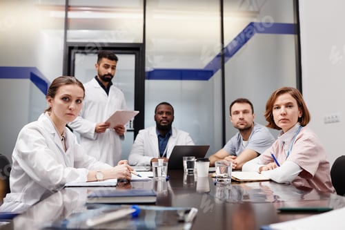 Preview: Group of intercultural medical experts in lab coats sitting by table