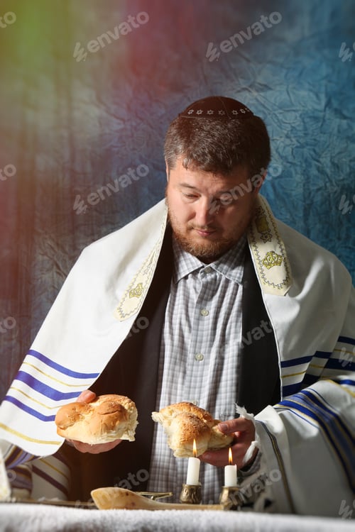Preview: Sabbath kiddush, man breaks Saturday's festive bread candlesticks with lit candles, and challah