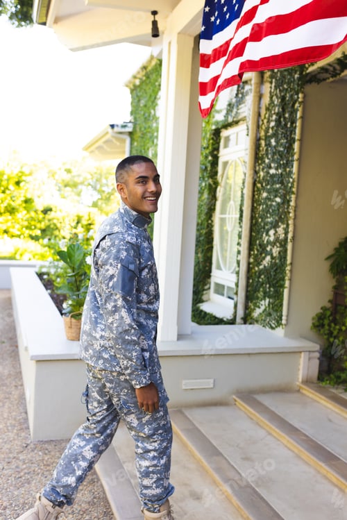 Preview: Happy biracial male american soldier wearing military uniform standing outside the house