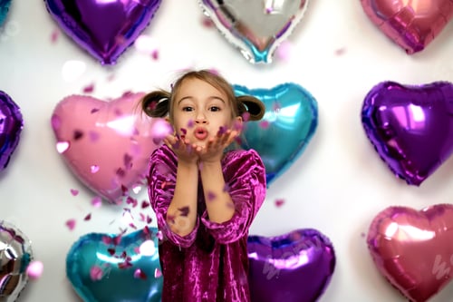 Vista previa: Kid blows confetti in the shape of hearts from palms while looking at the camera